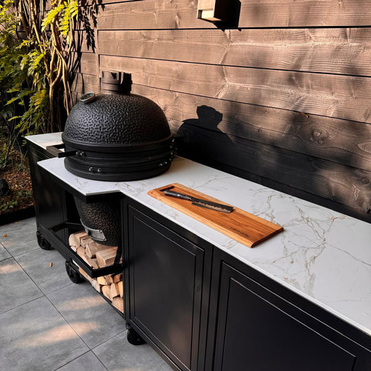 Luxe buitenkeuken met een zwarte Kamado BBQ, Dekton werkblad en op maat gemaakte zwarte kasten. Perfect voor buiten koken in een stijlvolle tuinsetting.